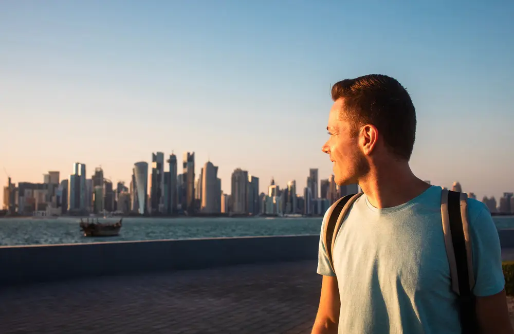 Govt updates travel advice level for key stopover point for Aussies 3 Solo male traveller in Doha, Qatar with city skyline in background as UN Tourism data shows regional recovery.
