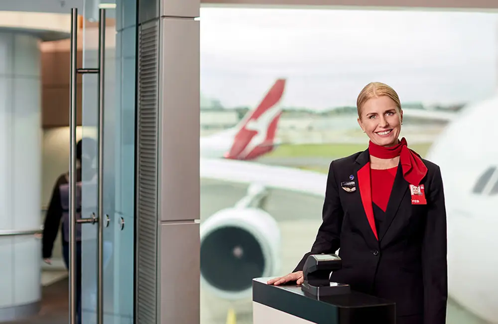 Flying paperless: Qantas takes off with first digital Australia Travel Declaration 2 Qantas flight attendant at airport terminal gate with aircraft seen outside window.