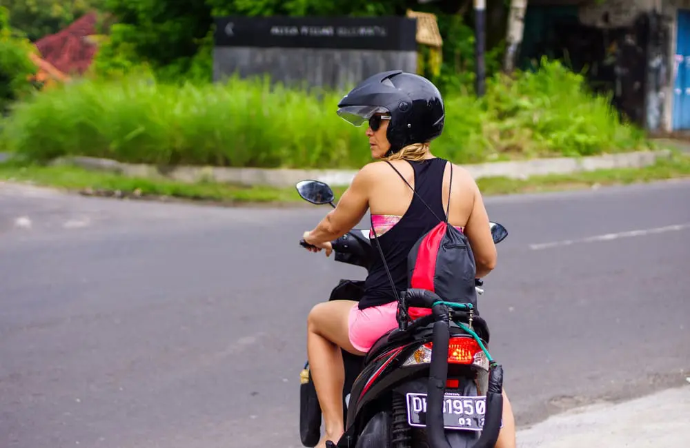 Female Russian tourist on scooter in Ubud, Bali stopped and waiting for traffic on road to avoid overseas scooter accidents.