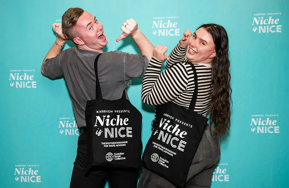 Evolution Travel Collective returns as Gold Plus Sponsor for Niche is Nice 2025 1 Two people pose against branded screen with branded bags at event.
