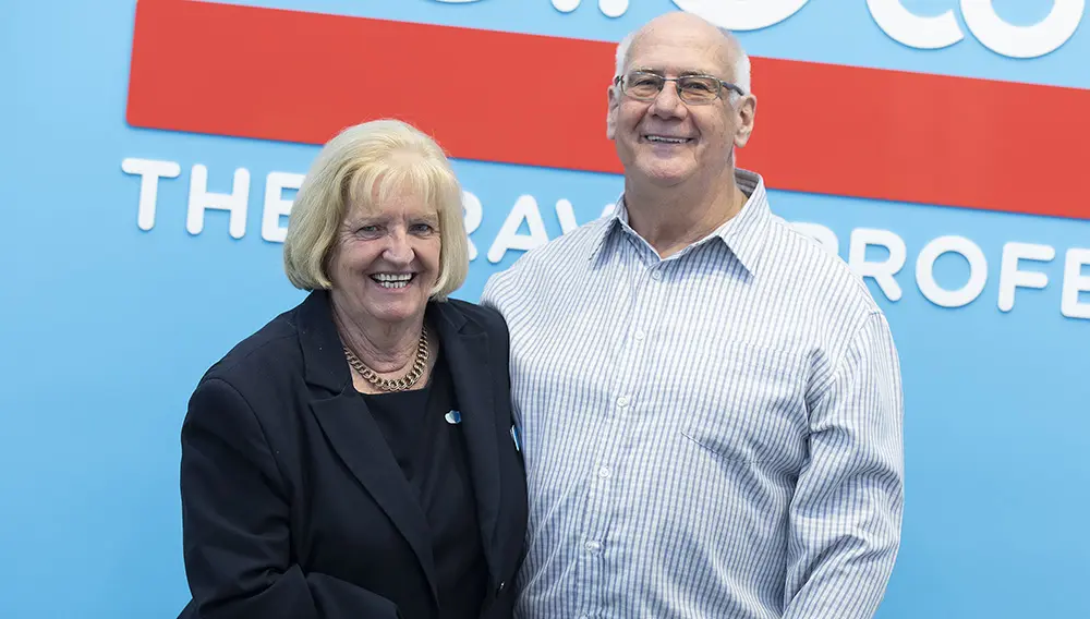 Previous Helloworld Travel Rowville owners Kath & John Williams outside store sign.