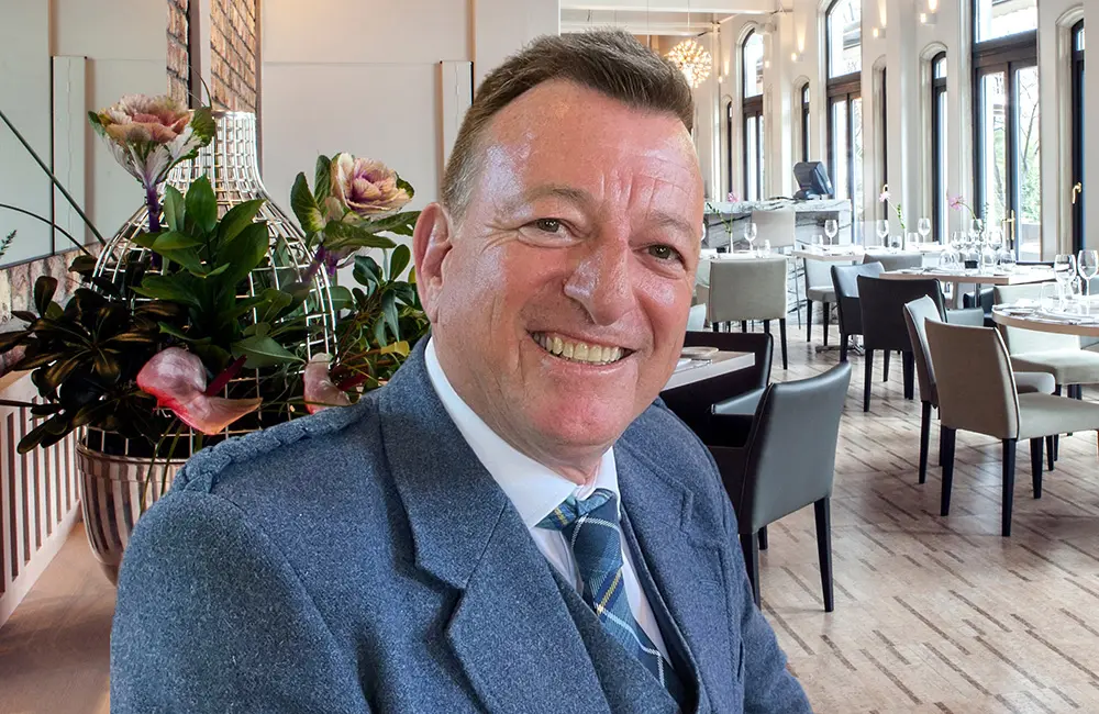 Movers + Shakers: MW Tours promotes David Reid as Director of Sales & Marketing 2 Close-up of man in suit in empty function area.
