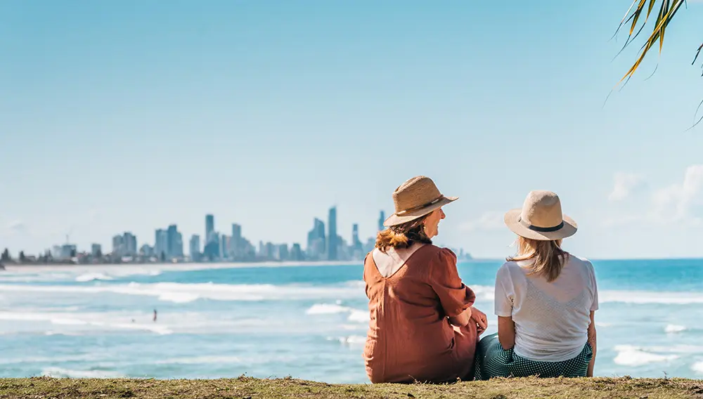 Two women sit on foreshore at Burleigh Heads National Park, Gold Coast. Image: TEQ for Gate 7 announcement