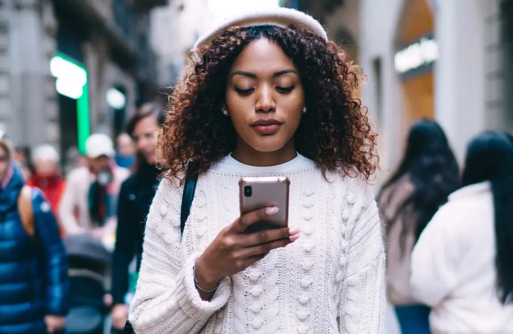 Female traveller in busy city street looking at her mobile phone – international roaming charges concept