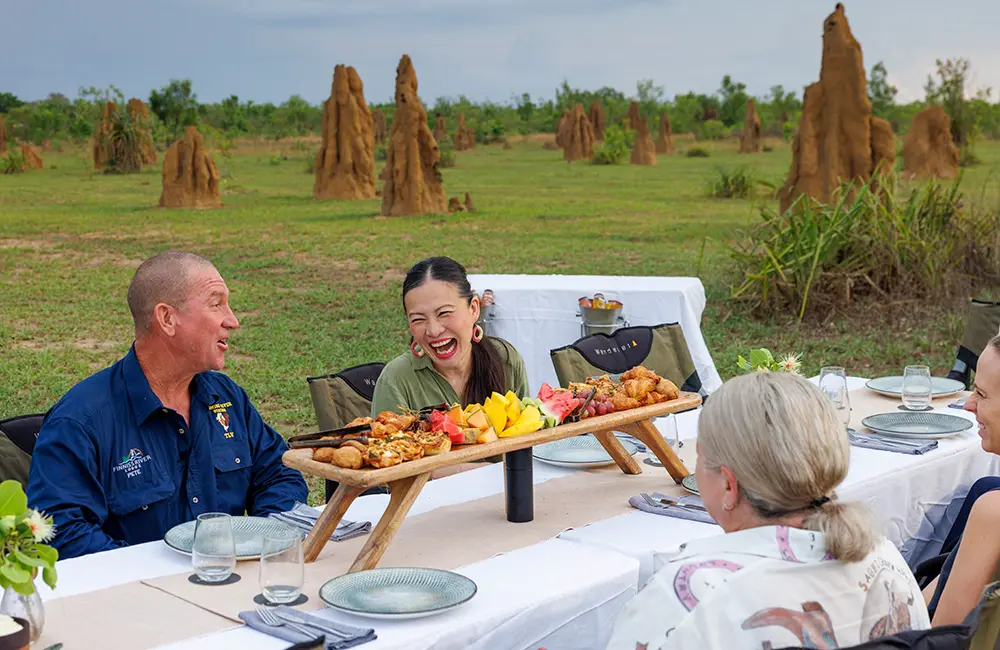 This familiar Aussie face is dishing the goods as the Northern Territory’s newest ambassador 4 People seated at long table outdoors with an array of local produce. Credit Toby Zerna for Tourism NT