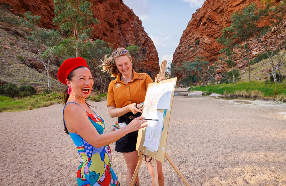 This familiar Aussie face is dishing the goods as the Northern Territory’s newest ambassador 3 Woman painting with guide at Simpsons Gap. Credit Toby Zerna for Tourism NT