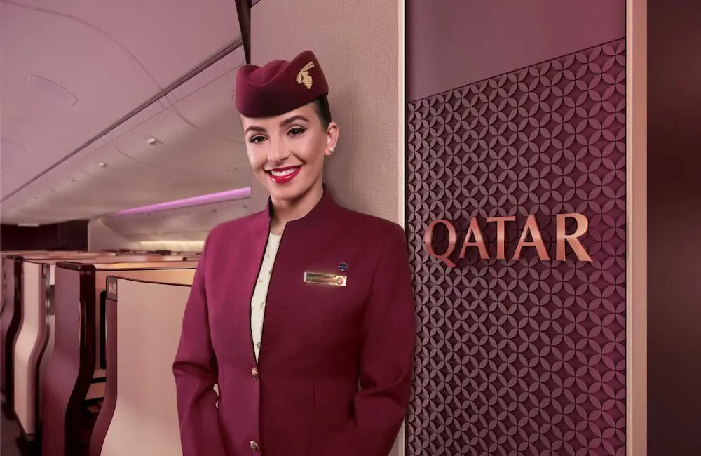 Qatar Airways female flight attendant at entrance of Qsuite business class cabin on B777 aircraft.