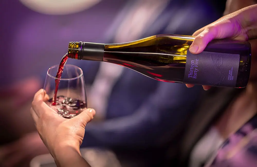Cheers to 85 years! Air New Zealand debuts wine label exclusively for flyers and members 1 Hand pouring pinot noir from Thirteen Forty Five bottle on Air New Zealand aircraft