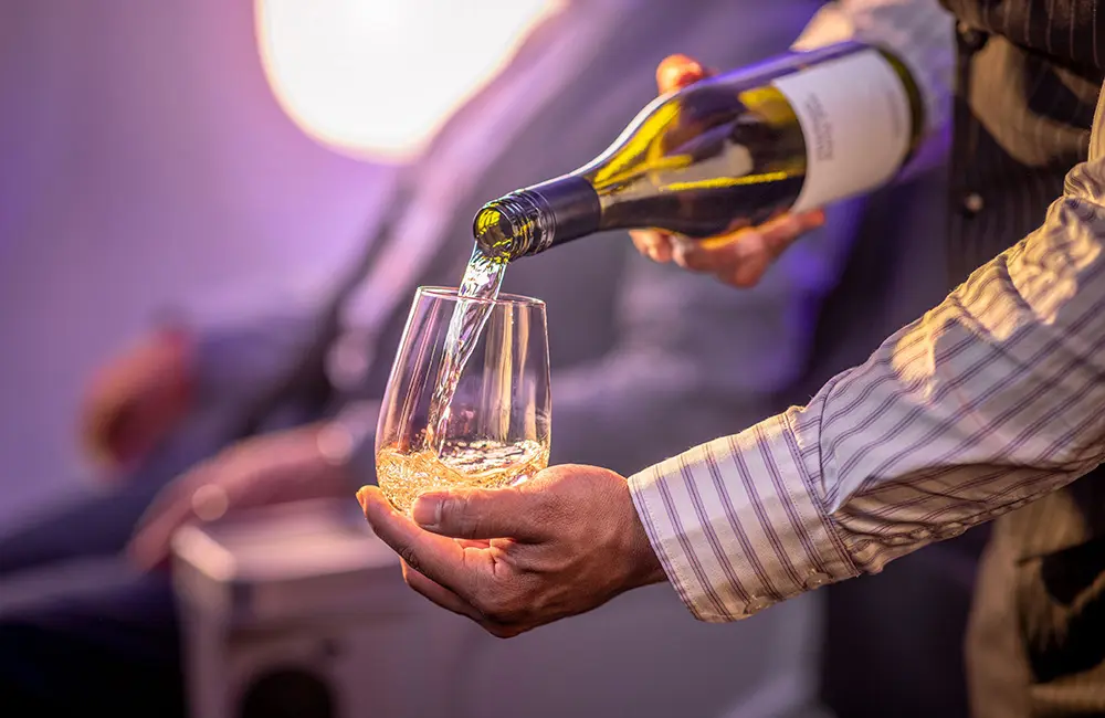 Air New Zealand drops trans-Tasman sale with one-way fares from just $265 for 85th year 1 Close-up image of male Air New Zealand flight attendant pouring wine into a glass in plane cabin.
