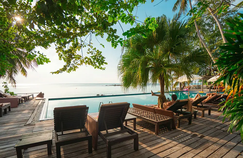 Travel insurance uptake ramps up as Aussies prioritise peace-of-mind over cost-of-living 1 People lounging on deck chairs near a resort pool – travel insurance.