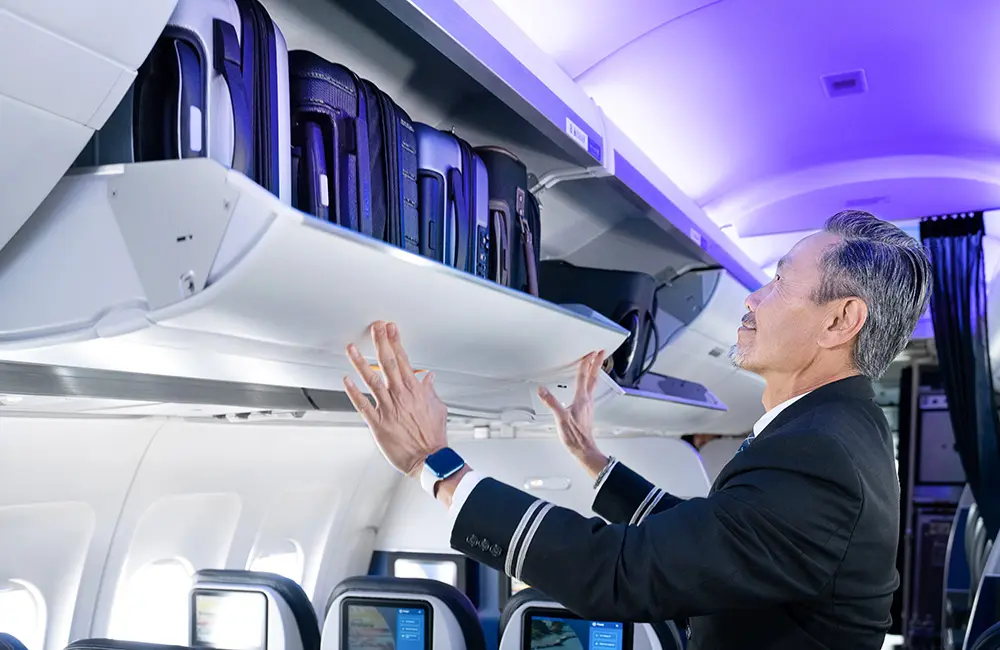 United Airlines just saved Aussie travellers 45 minutes on US connections 2 United Airlines male flight attendant closing overhead bin on plane.