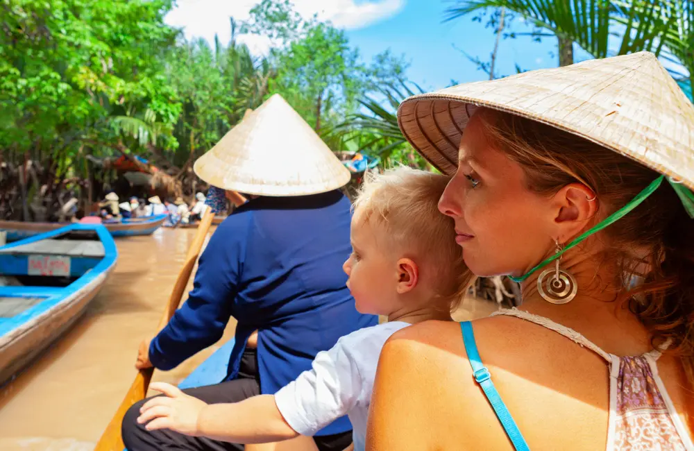 Triple UK & double US: Japan travel surges as total outbound trips grow by 8% 2 Happy family ride on traditional Vietnamese boat by yellow brown water in canal. Mekong river delta