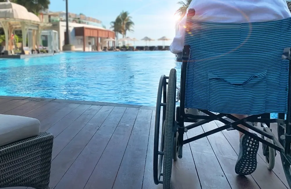 Person in wheelchair by pool recuperating after an accident overseas. Travel insurance