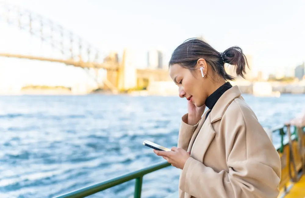 ATO targets bleisure trips: Corporate Traveller warns Aussies to tread carefully this tax season 1 Businesswoman with airpods & smartphone travelling on Sydney ferry, Sydney Harbour Bridge in background
