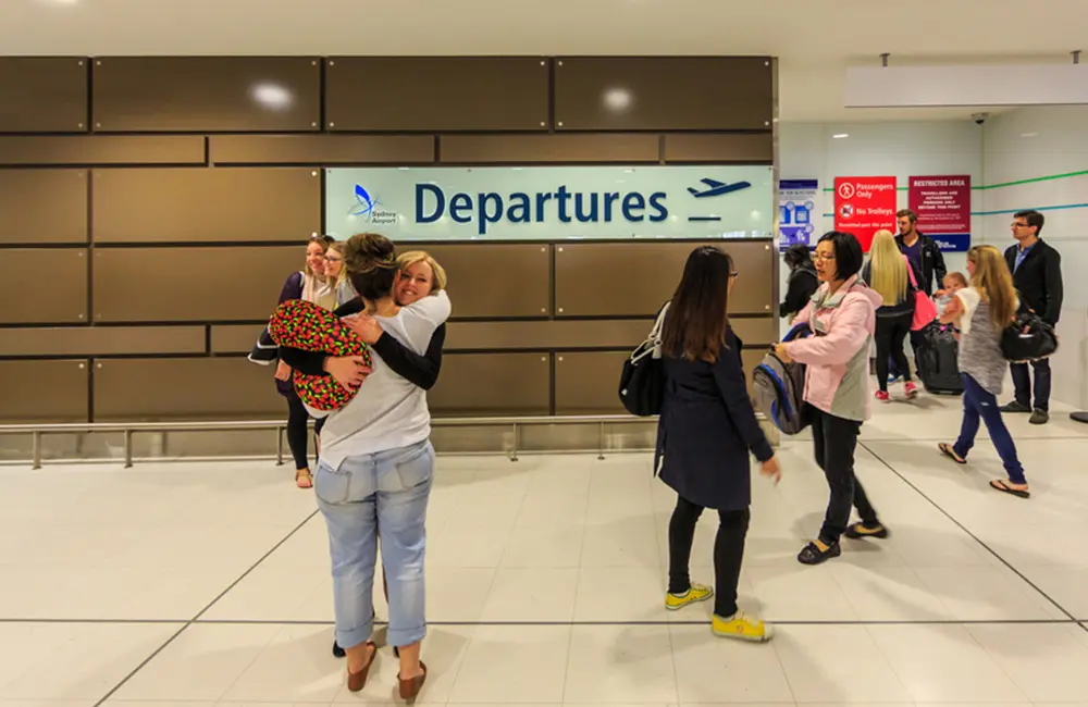 Brisbane Airport records busiest ever day; Sydney Airport gears up for record holiday period 2 People hug goodbye at departures sign at Sydney Airport.