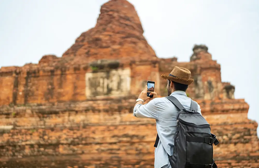 2 in 3 Aussies say rising costs are impacting travel plans – well above the global average 2 Male tourist taking a smartphone photo of temple ruins in Ayutthaya Province, Thailand. Image: Getty Images