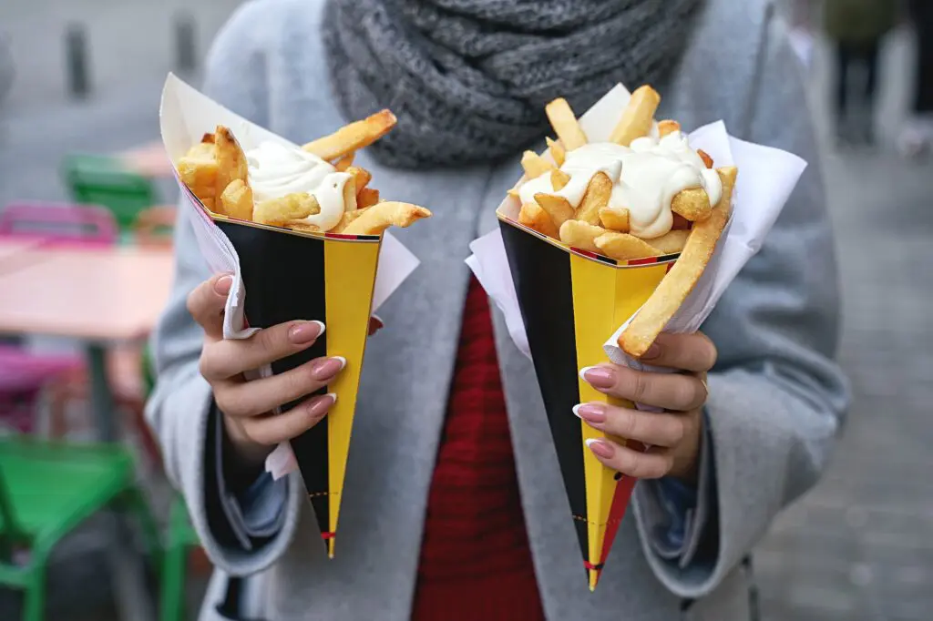 DFAT gives new travel advice level for popular western European nation 1 Belgian frites or french fries with mayonnaise in Brussels, Belgium. Female tourist holds two portions of fries in hands in the street.