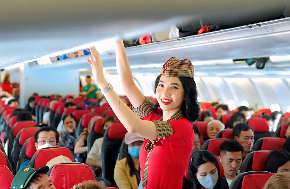Airline flying to four Aussie hubs drops international base fares by 100% 1 Female flight attendant in Vietjet aircraft cabin with seated customers.