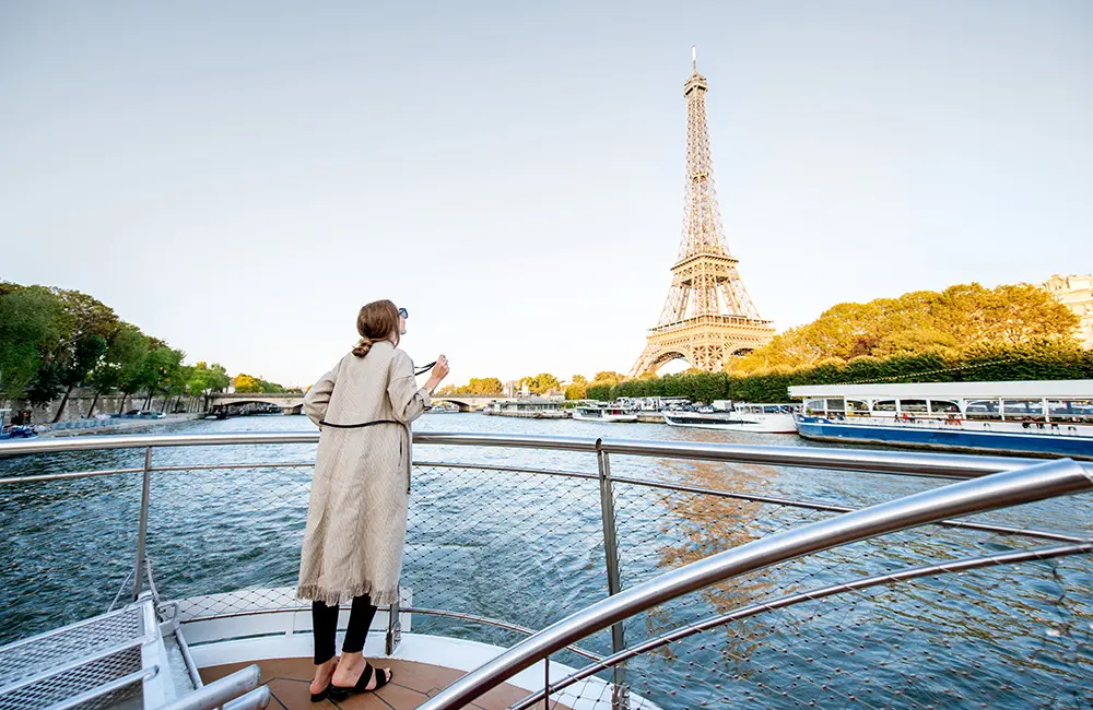 Young woman enjoying beautiful landscape view on the riverside with Eiffel tower from the boat during the sunset in Paris. Wide view with copy space – travel intent