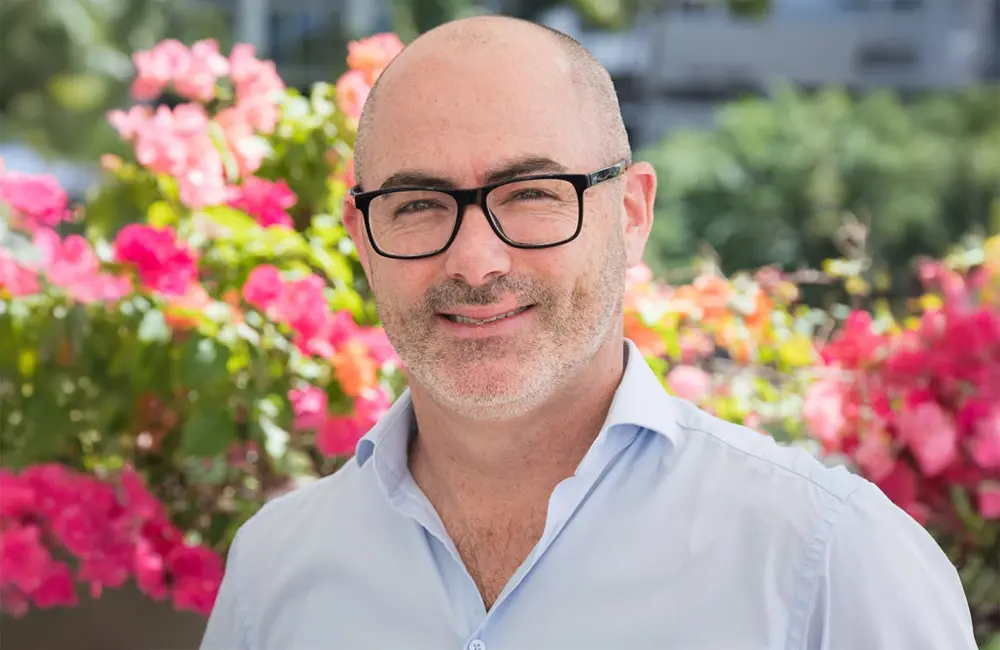 Corporate headshot of man against floral background outdoors.