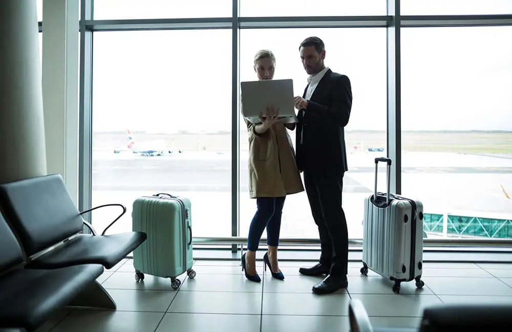 Game-changer alert: 1000MTG Founder launches Adamaz Travel with big solutions for small agencies 1 Businesspeople look at laptop with suitcases at airport – Adamaz Travel solutions.
