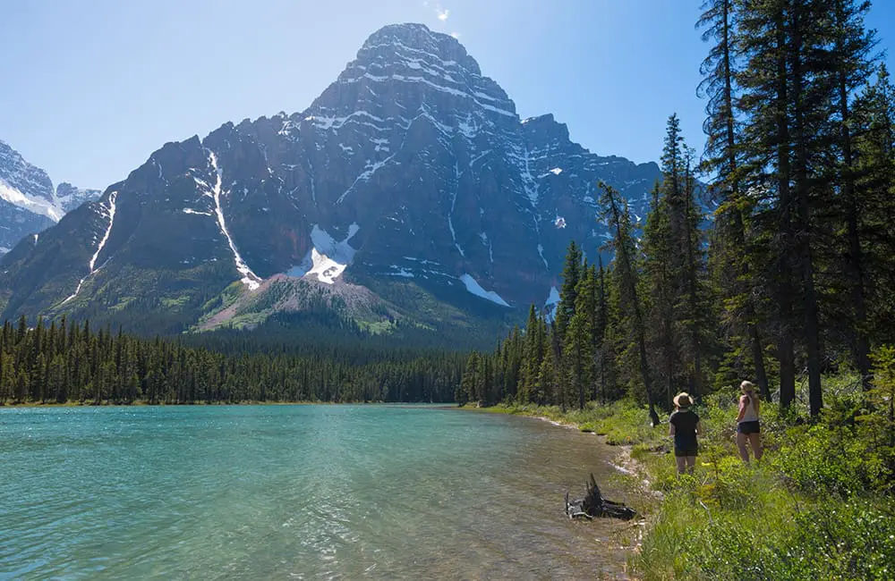 Free admission & discounted camping: This Parks Canada offer is too good to pass up 1 Two women walking at edge of lake in Banff National Park – Parks Canada. Image: William Patino