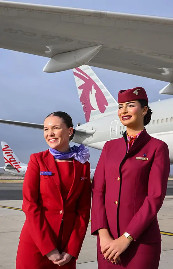Virgin Australia debuts first Perth–Doha flights with one-stop Europe access for WA flyers 1 Virgin Australia flight attendant and Qatar Airways flight attendant on tarmac in front of planes. Image: James D. Morgan from Getty Images