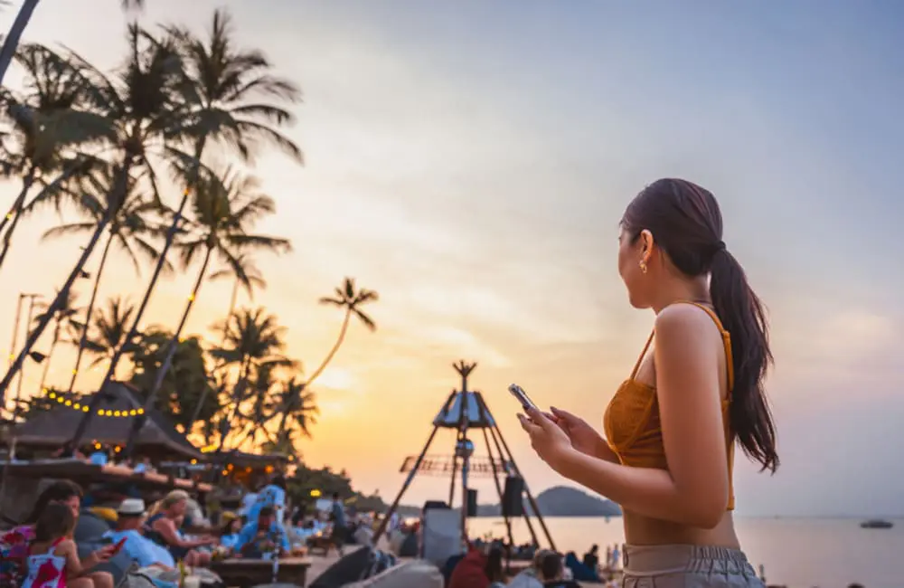 Woman at beach festival holding smartphone – AI travel recommendations