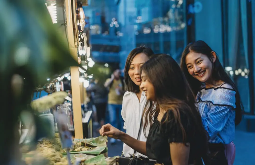 AI vs influencers: Which is more trusted for travel recommendations? 3 Group of female friends at outdoor street food market – AI travel recommendations