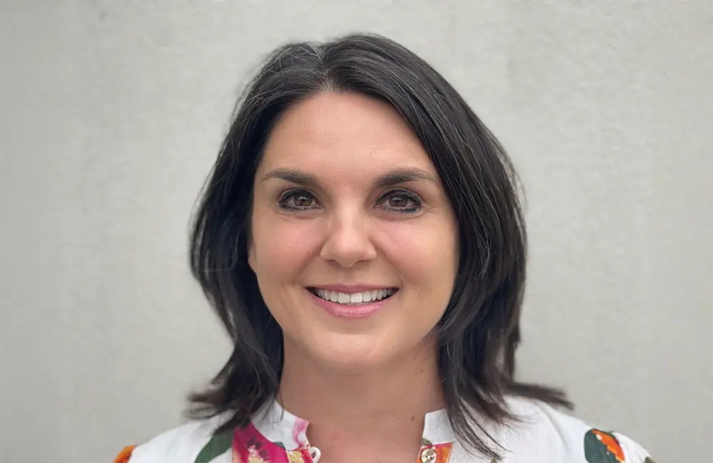 Corporate headshot of woman against plain background.