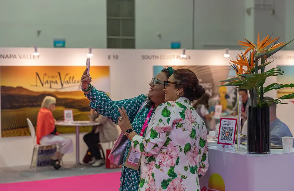 Two women taking a selfie in front of a booth at ILTM Asia Pacific 2025 in Singapore