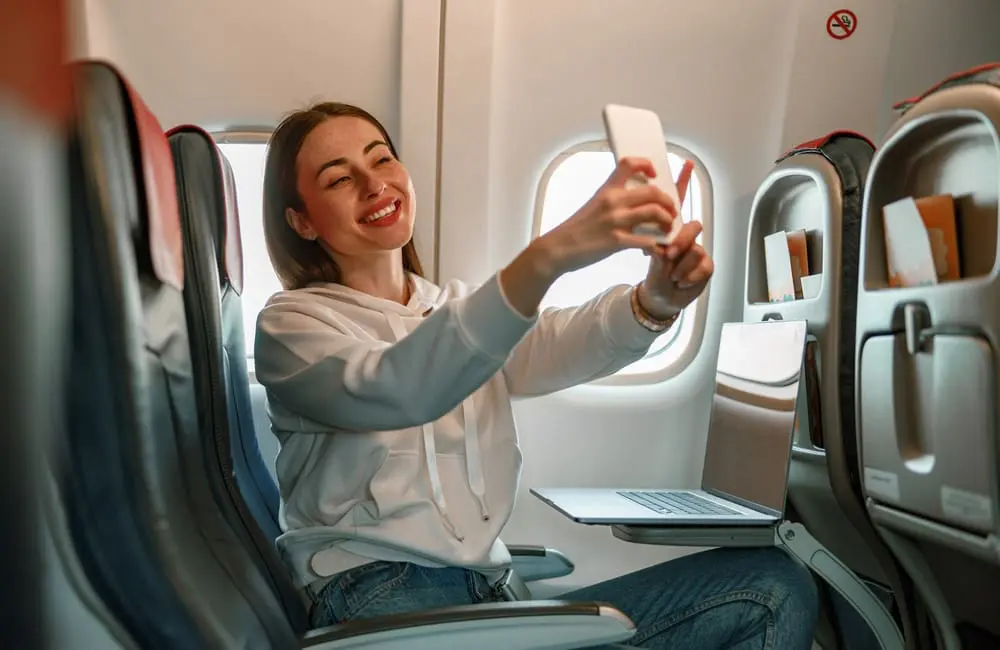 Most Aussies say this is the best time to fly overseas – and it’s not what you’d expect 2 Female plane passenger taking selfie – preferred times for flying overseas. Image: Shutterstock