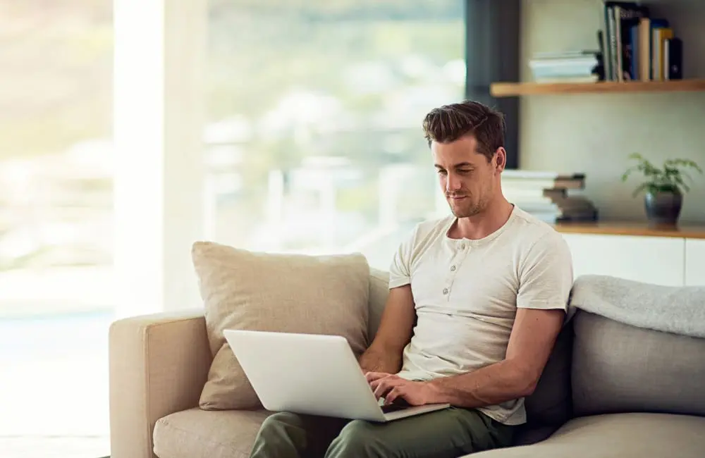 Work hard, holiday harder: 1 in 3 Aussie bosses now approve workations 1 Man sitting on couch using laptop – workations trend. Image: Shutterstock