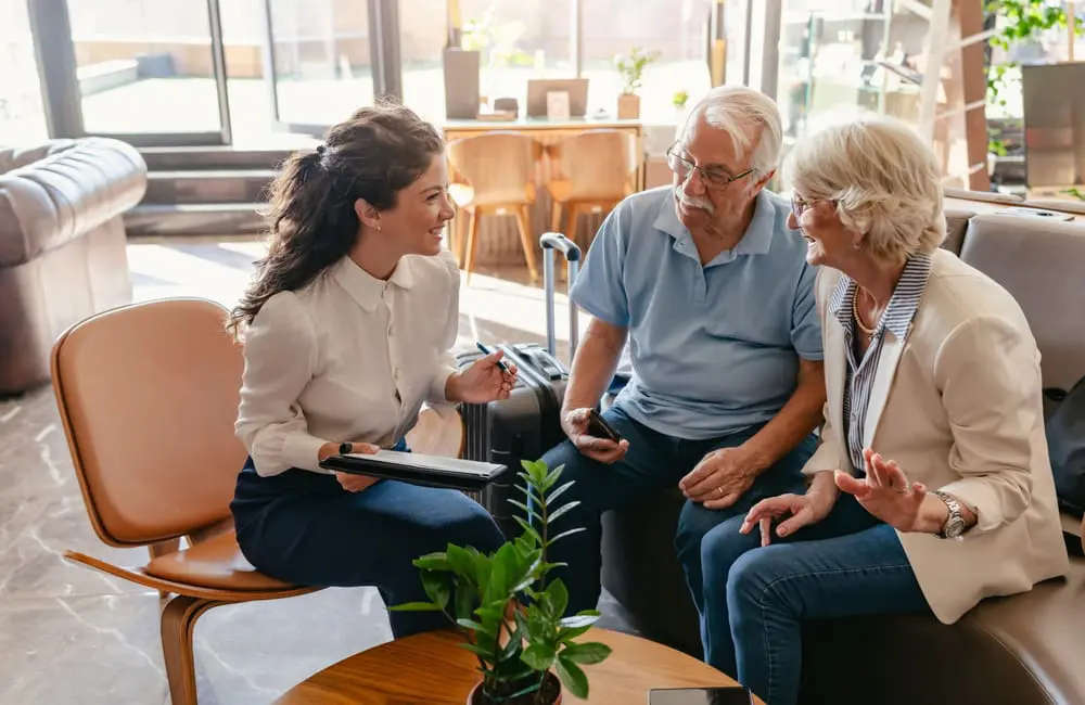 3 in 10 Aussies now use AI to book holidays with sharp uptake by this surprising source 2 Boomer couple sit with hospitality team member to check-in via tablet – use AI to book holidays
