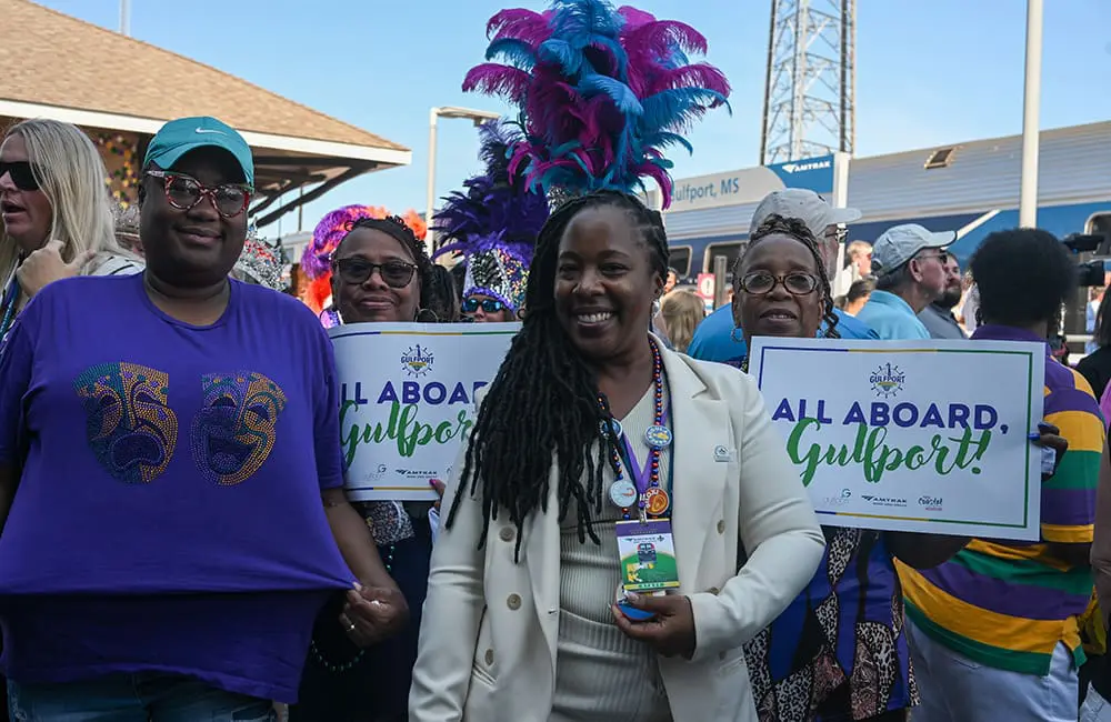 Carnival on track! Amtrak restores Mardi Gras Service between New Orleans & Mobile 3 Women holding Gulfport signs for the Amtrak Mardi Gras Service. Image: Larry Everage Jr