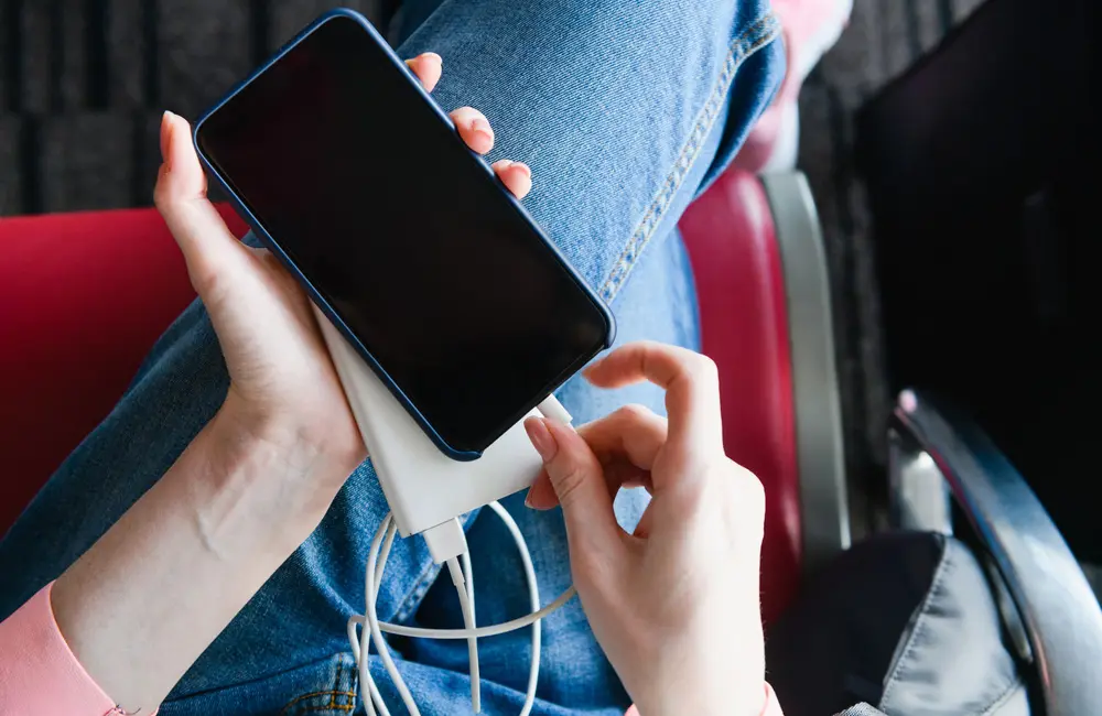 Top-down shot of woman using portable power bank charger with smartphone at airport.