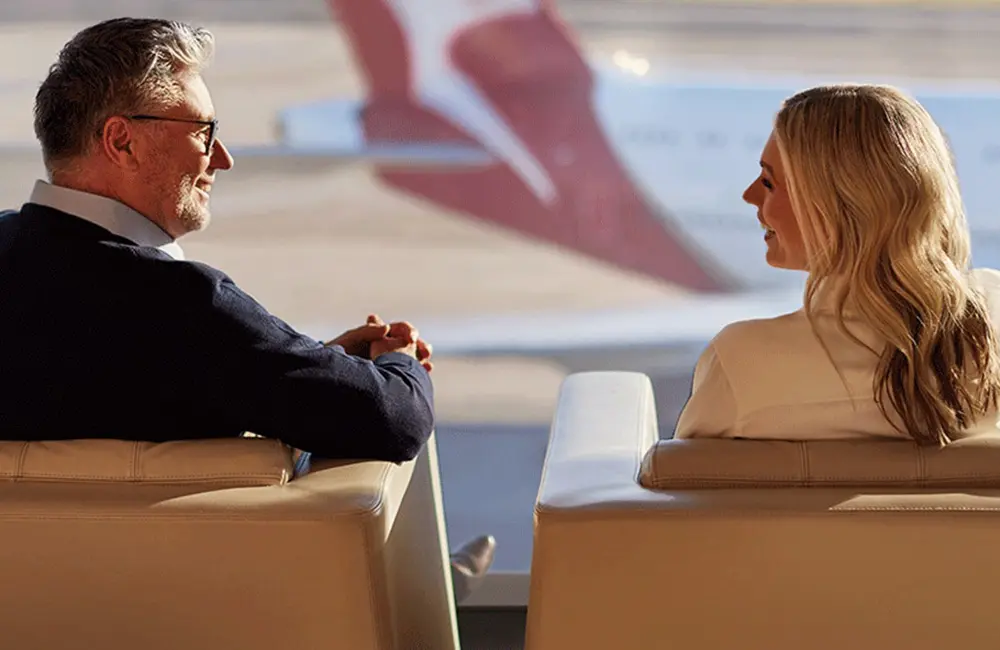 Qantas goes daily for the first time on Sydney-New York via Auckland flights 3 Male and female corporate travellers in Qantas lounge with aircraft in window