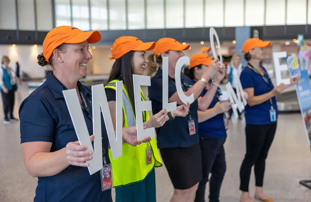 Newcastle goes international again with first-ever Jetstar Bali flight; drops 24-hour sale 2 NTL team hold letters spelling 'Welcome' inside terminal.