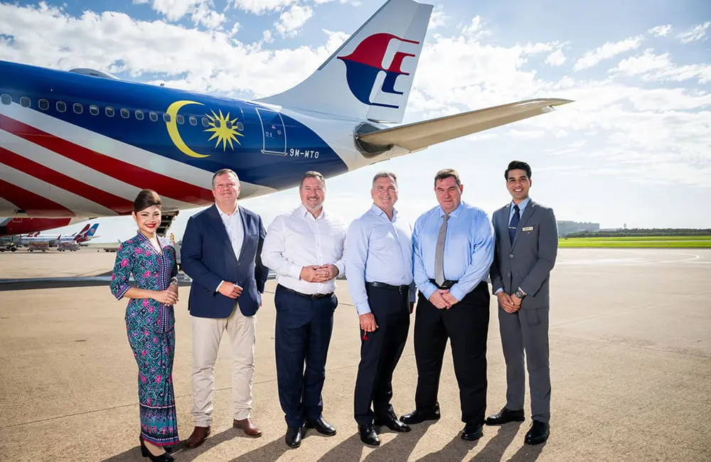 Brisbane Airport Corporation and Malaysia Airlines executives on tarmac with aircraft tail in background.