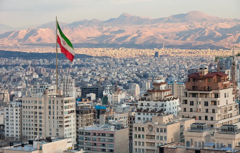 Waving Iran flag above skyline of Tehran at sunset.
travel alert