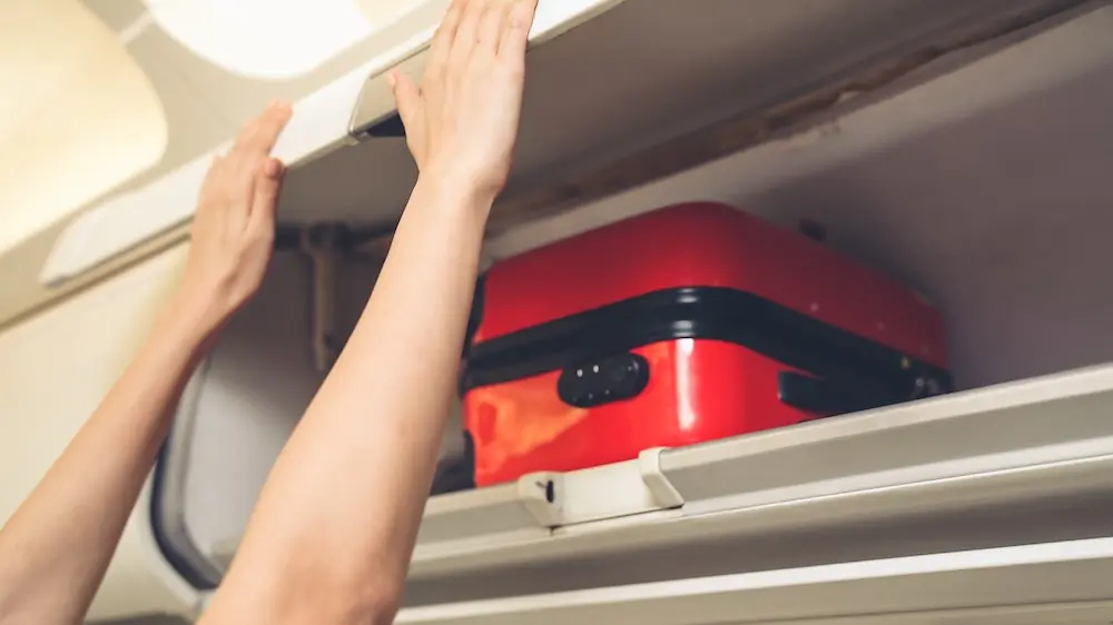 Cabin crew lift luggage bag in airplane . Airline transportation and tourism concept.