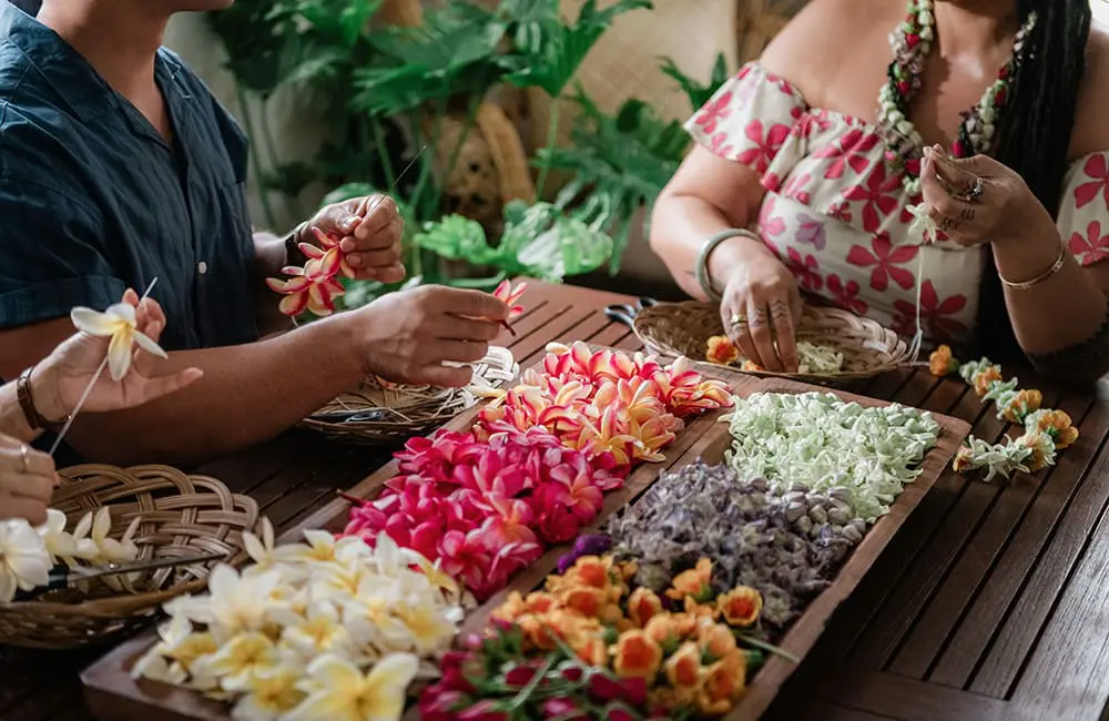 People making lei wreaths with tropical flowers in Maui. Image: HTA