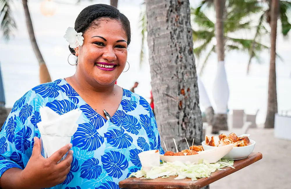 Fijian women holds plate of food on the beach. Image: Brook Sabin Fiji Matai Specialist 
