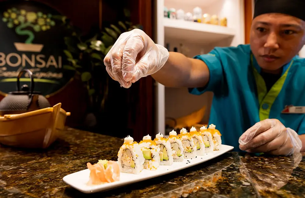 Chef putting finishing touches on sushi dish at Bonsai Sushi Express on Carnival Encounter.