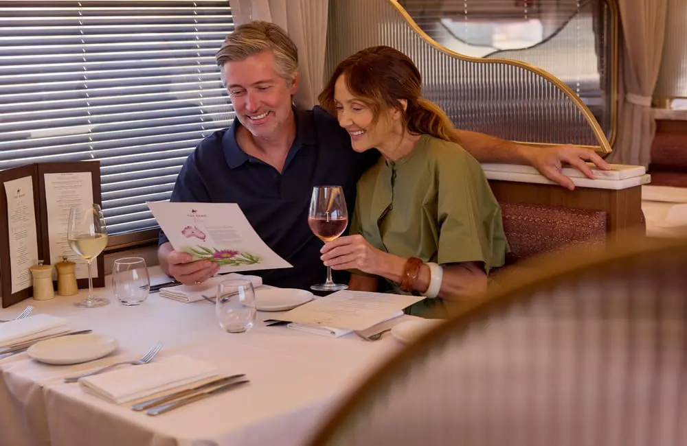 Couple with wine looking at menu on board The Ghan rail journey in Gold Premium.