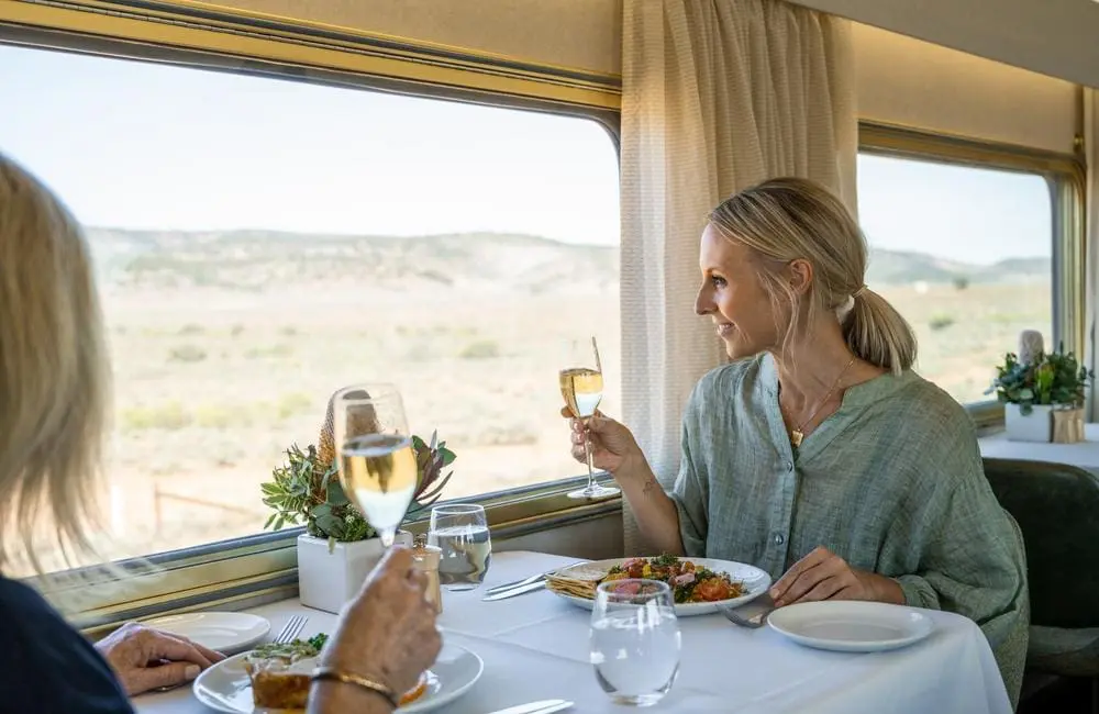 Two female passengers with meals and wine look out the window on The Ghan.