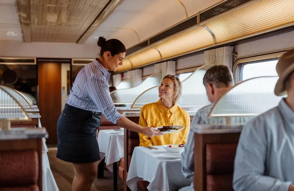 Wait staff serving passengers in dining car The Ghan Gold Premium rail travel features gourmet dining