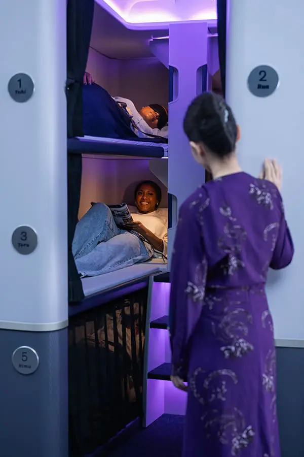 4-hour nap for $495: Air New Zealand’s innovative Economy Skynest sleep pods on sale from 18 May 5 Flight attendant with passengers in Air New Zealand Economy Skynest sleep pods.