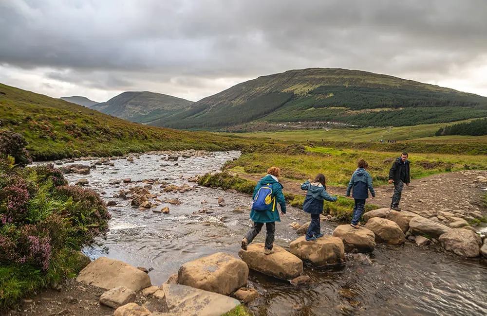 Family group walking across stones at the Fairy Pools on Scotland's Isle of Skye. Image: Intrepid Travel
