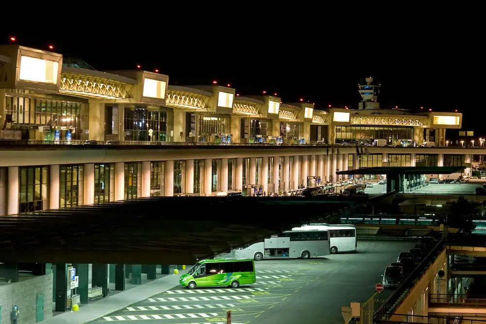 DFAT warns EES is causing up to 6-hour delays at European airports - what travel advisors are saying 2 Night photo of Milan Malpensa Airport Terminal 1, control tower and parking